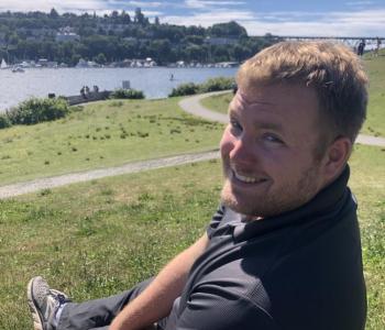 Matthew Childs sits outside on a hill overlooking a body of water.