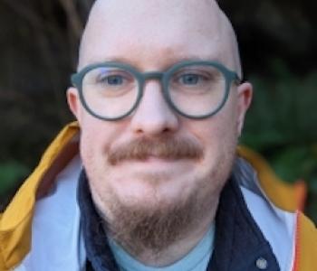 Matthew Poland looks at the camera while wearing green glasses.