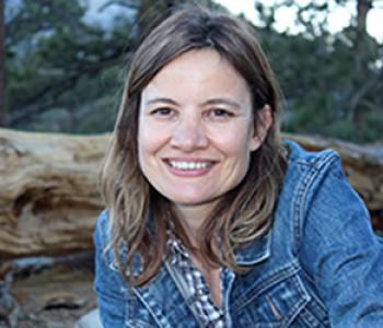 Minda Martin sits outside wearing a denim jacket and patterned shirt. 