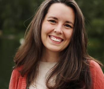 Sarah Moore stands outside while wearing a read cardigan and white shirt.