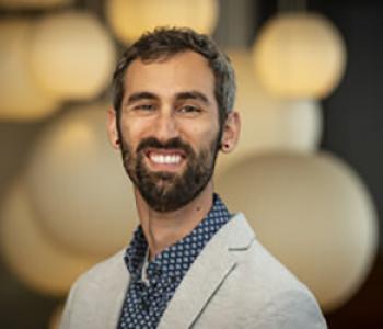 Daniel Stofleth wears a light jacket and a collared shirt while standing in front of blurry lit globes.