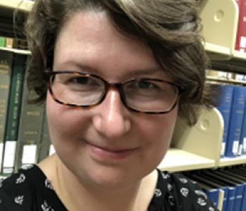 Verena Kick stands in front of a bookcase wearing glasses and a dark shirt.