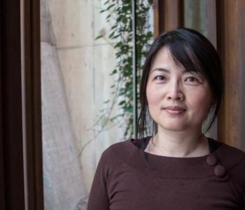 Ping Wang stands in front of a window wearing a brown shirt.