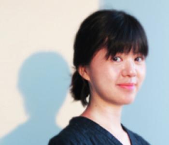 Ying-Hsiu Chou stands in front of a white wall wearing a dark shirt.