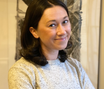 Rachel Arteaga smiling at the camera in a grey sweater, arms folded.