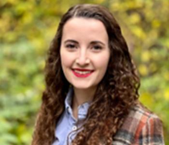 Laura Gehrke stands outside wearing a blue collared shirt and plaid jacket.