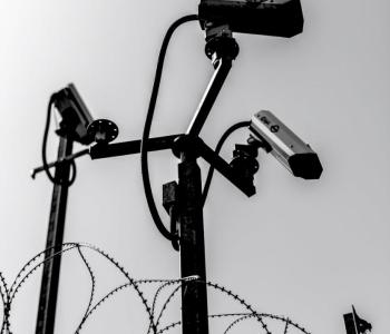 Three surveillance cameras atop barbed wire and spiked poles