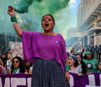 Photo of an Indigenous woman with her arm raised chanting at a rally in front of other women