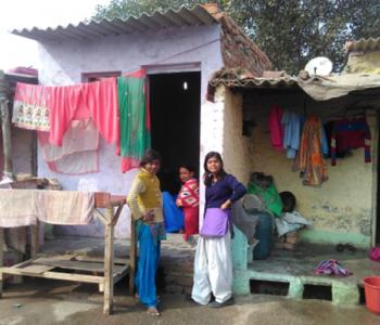 Three women sit or stand near a building's doorway with colorful laundry hanging around them.